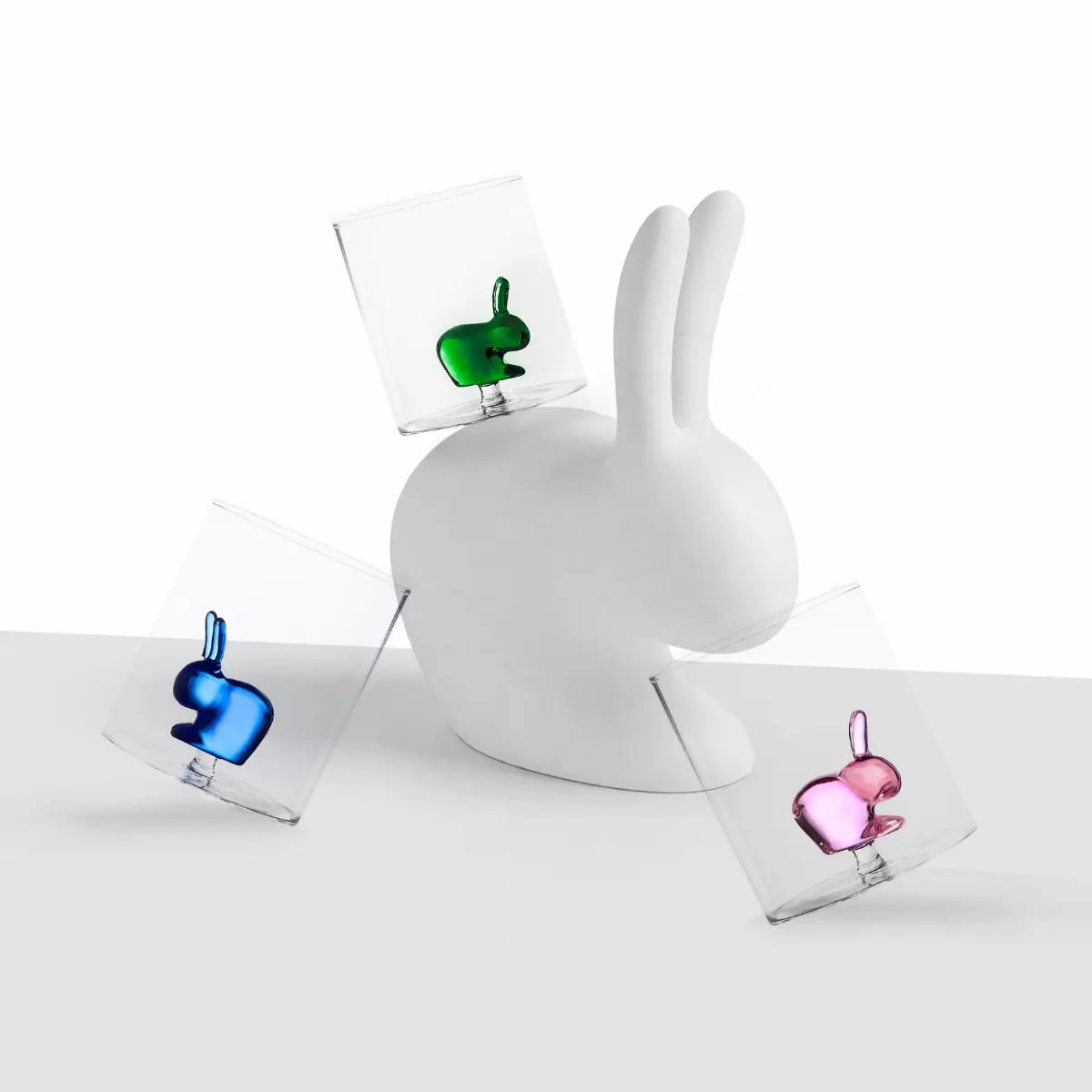 Bicchiere in vetro con coniglio della collaborazione Qeeboo x Ichendorf appoggiati intorno a fermoposta rabbit bianco di Qeeboo