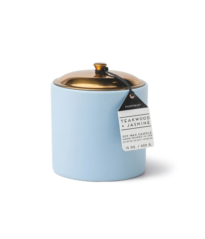 Portacandele azzurro, tappo in metallo color oro. Etichetta scritta teakwood e jasmine. Fondo bianco