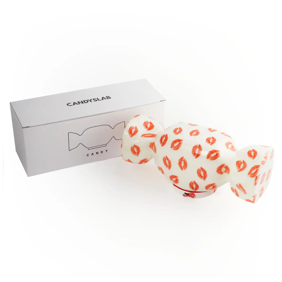 Confezione bianca con scritte e disegni neri e lampada da tavolo a forma di caramella con base bianca e fantasia con baci rossi. Sfondo bianco 