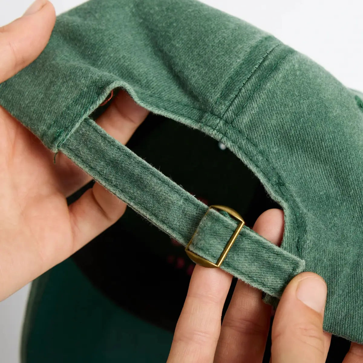 Dettaglio della chiusura regolabile del cappellino verde. Mani che tengono il cappellino.