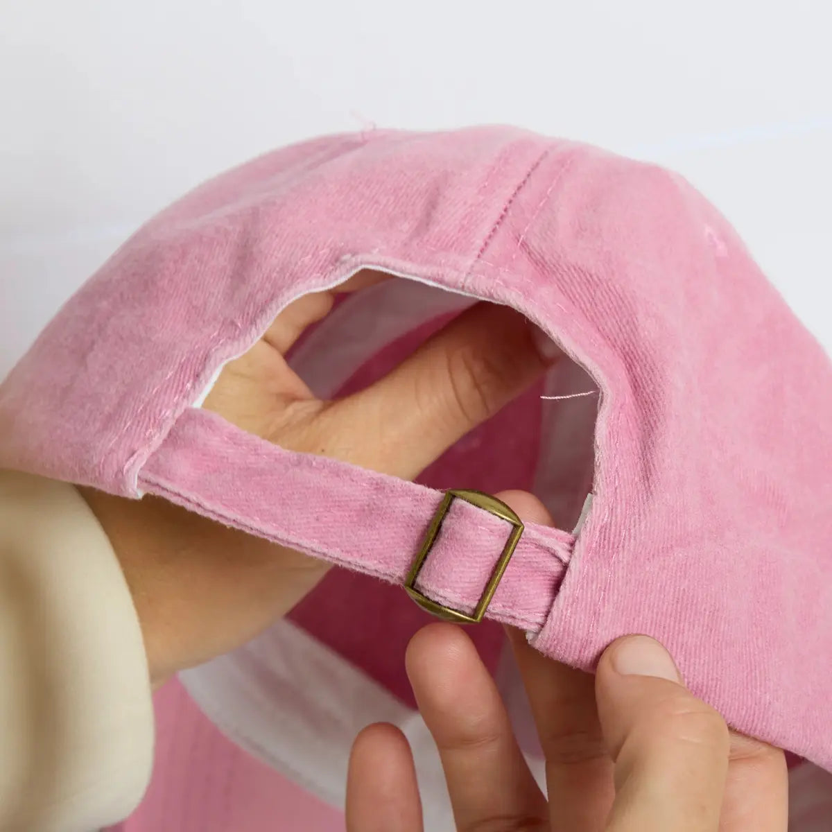 Mani che tengono il cappellino rosa e mostrano il dettaglio del gancio per regolare il cappellino 