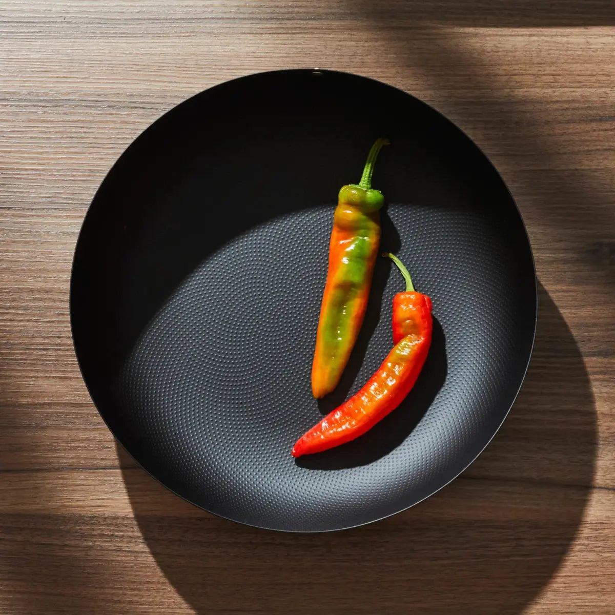 Cestino tipo fruttiera in acciaio nero con puntini a rilievo con due peperoncini freschi
