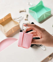 Mano che tiene la ciotola da viaggio pieghevole rosa con altre ciotole colorate sullo sfondo.