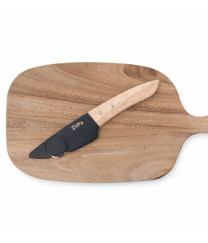 Coltello con lama e rotella in acciaio nera e manico in legno. Appoggiato su tagliere in legno. Sfondo bianco.