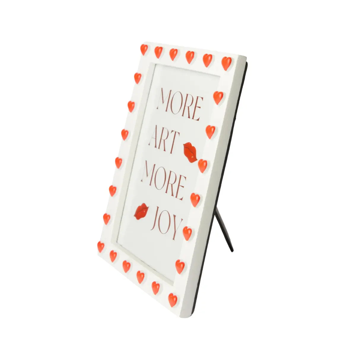 Vista laterale di una cornice rettangolare portafoto. Bordo bianco con cuori in rilievo rossi. All'interno stampa con scritto more art more joy. Sfondo bianco
