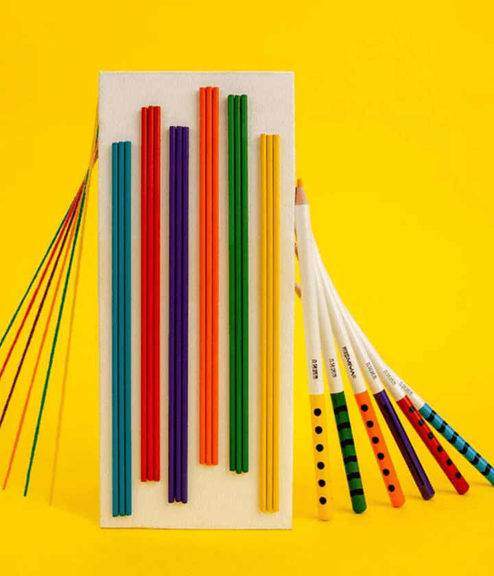 Rettangolo con righe colorate e matite appoggiate lateralmente. Immagine su sfondo giallo.