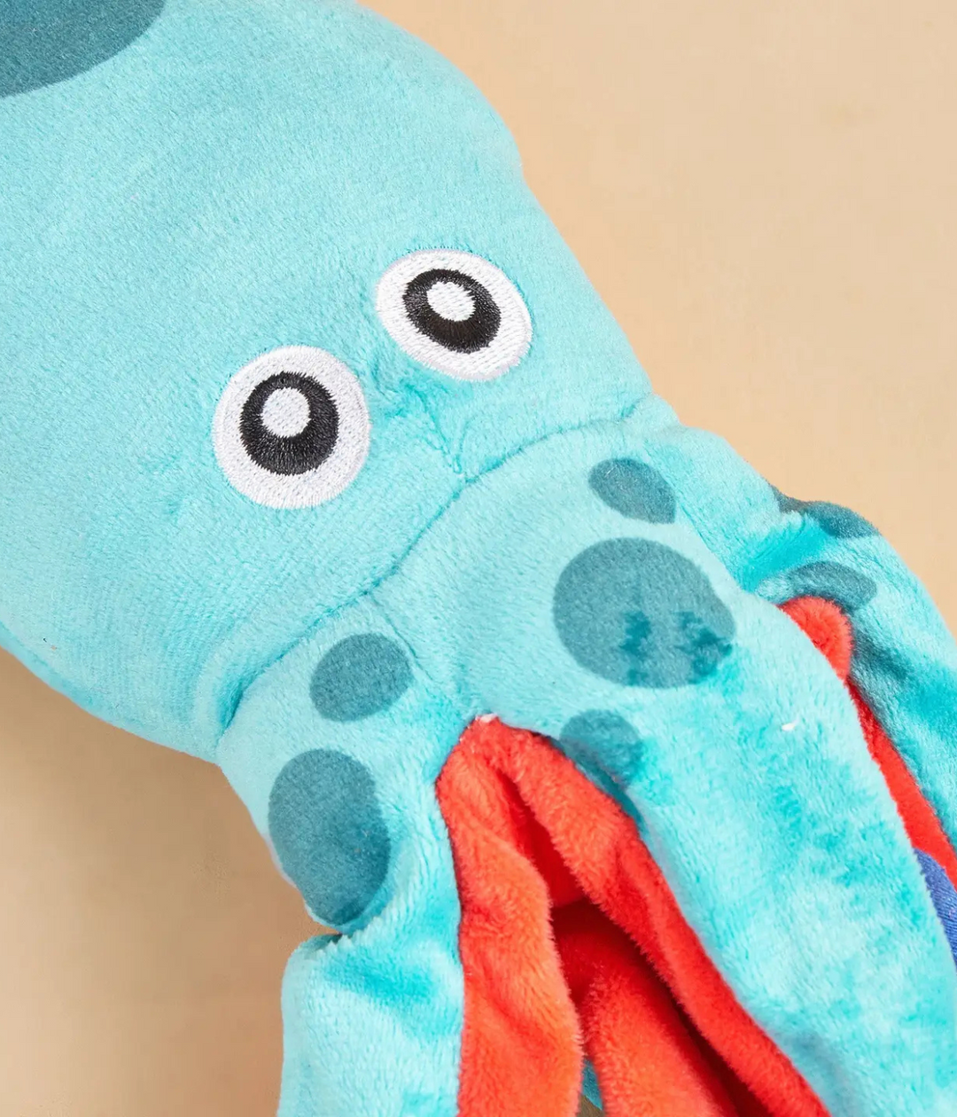 Dettaglio muso peluche polpo. Azzurro e rosso con occhi neri. Sfondo beige