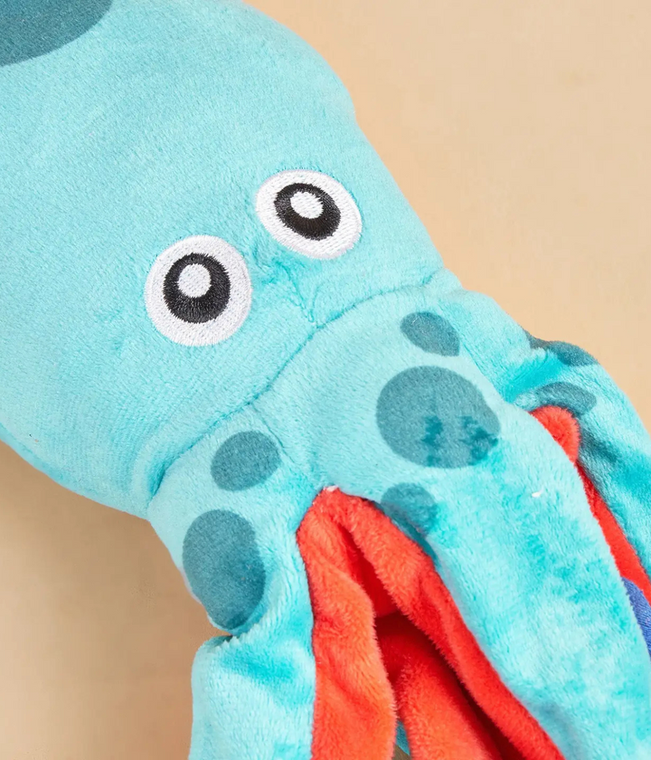 Dettaglio muso peluche polpo. Azzurro e rosso con occhi neri. Sfondo beige