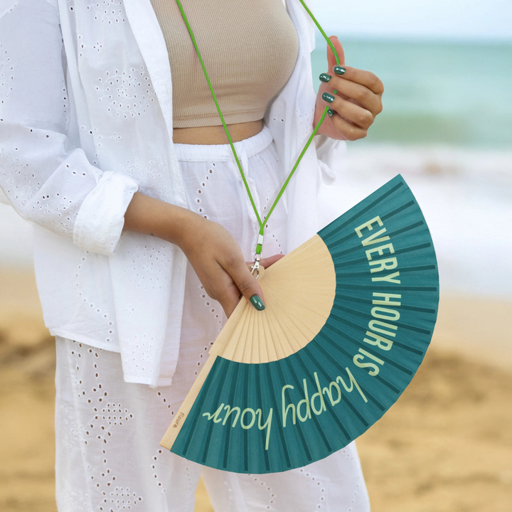 Donna in spiaggia con appeso al collo il ventaglio Every hour is happy hour , laccetto verde.