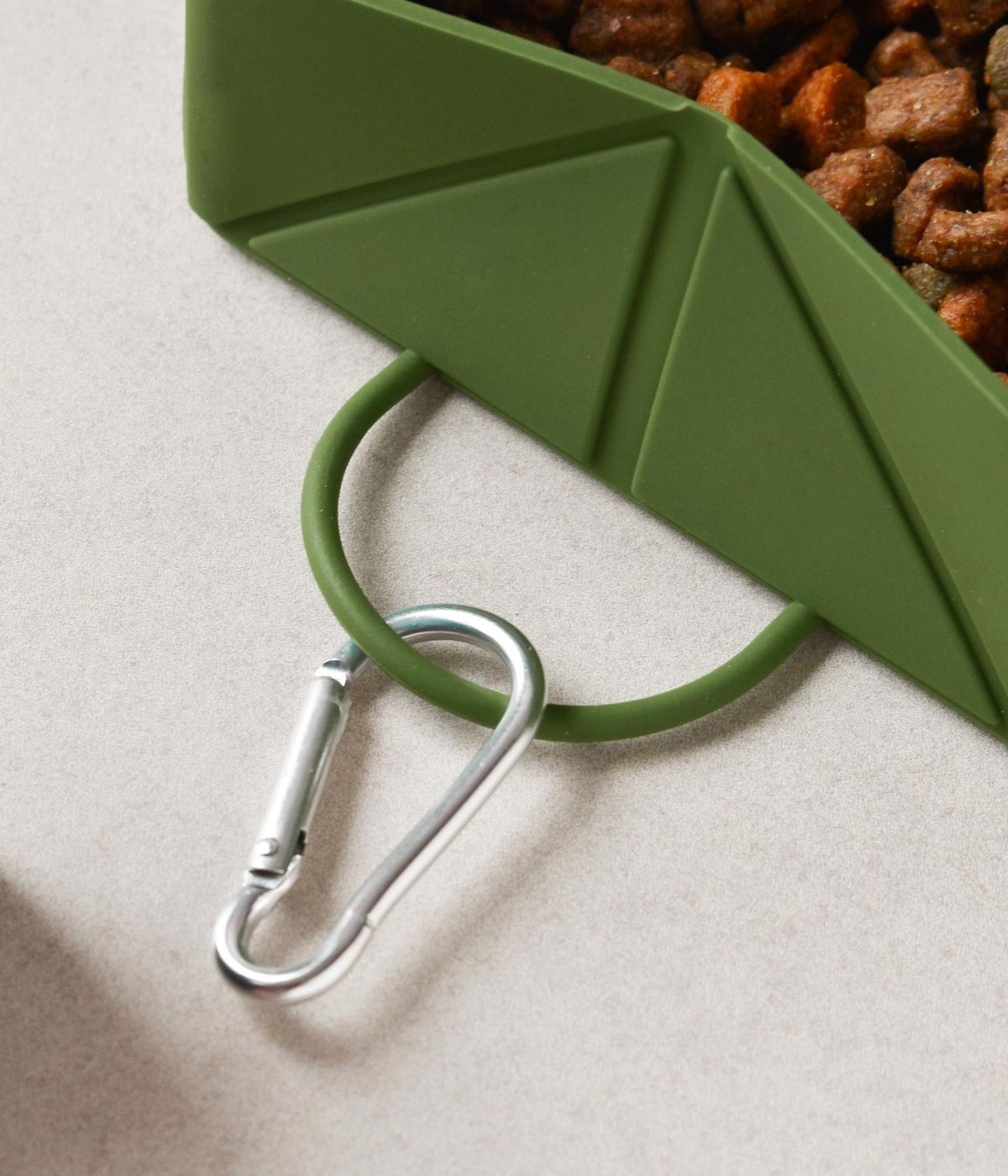 Dettaglio moschettone ciotola pieghevole verde con croccantini cane. Sfondo bianco