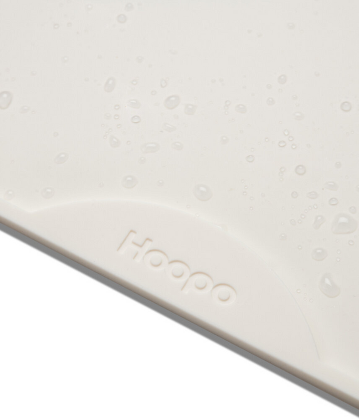 Gocce d'acqua su tappetino in silicone bianco con scritta Hoopo. Sfondo bianco