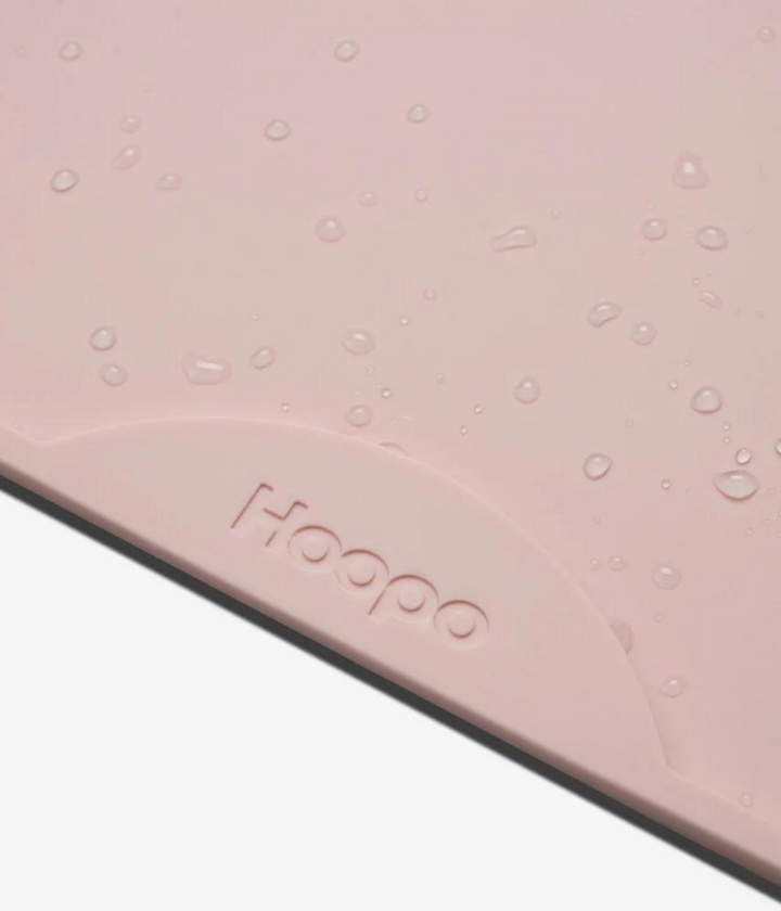Gocce d'acqua su tappetino in silicone rosa con scritta Hoopo. Sfondo bianco