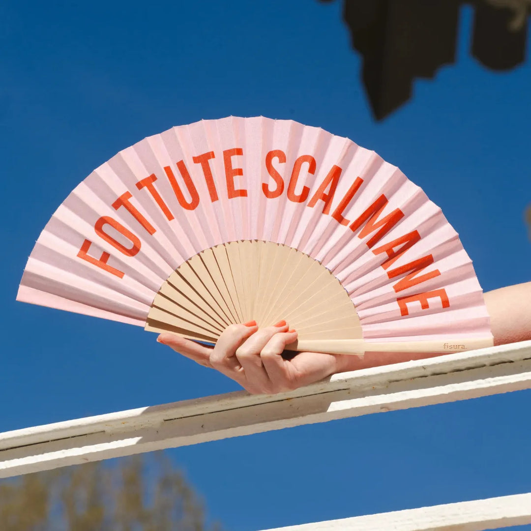 Mano che tiene ventaglio rosa fottute scalmane con sullo sfondo il cielo azzurro. 