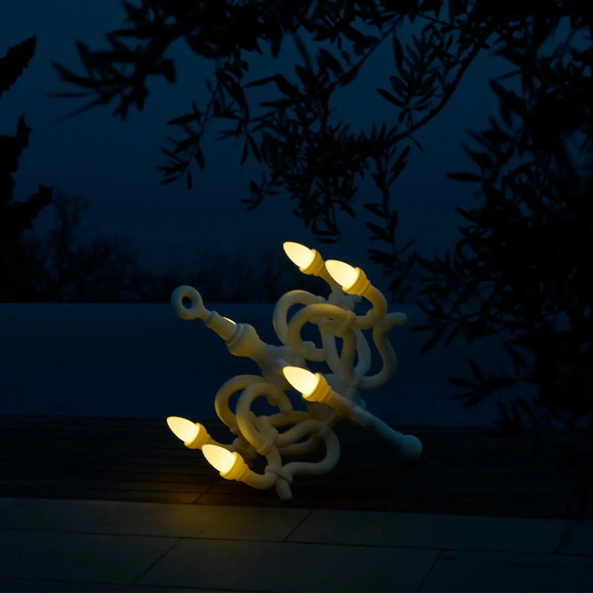 Lampada da terra a forma di candelabro classico appoggiata a terra. L'ambiente è notturno e le 6 lampadine led sono accese e fanno una luce d'ambiente soffusa