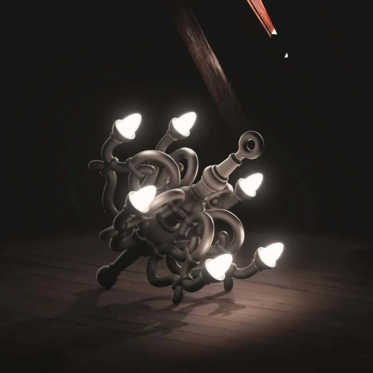 Lampada da terra nera a forma di candelabro classico. La lampada è appoggiata a terra su un pavimento di legno scuro. L'ambiente è scuro e le 6 lampadine sono accese e fanno una luce soffusa nell'ambiente