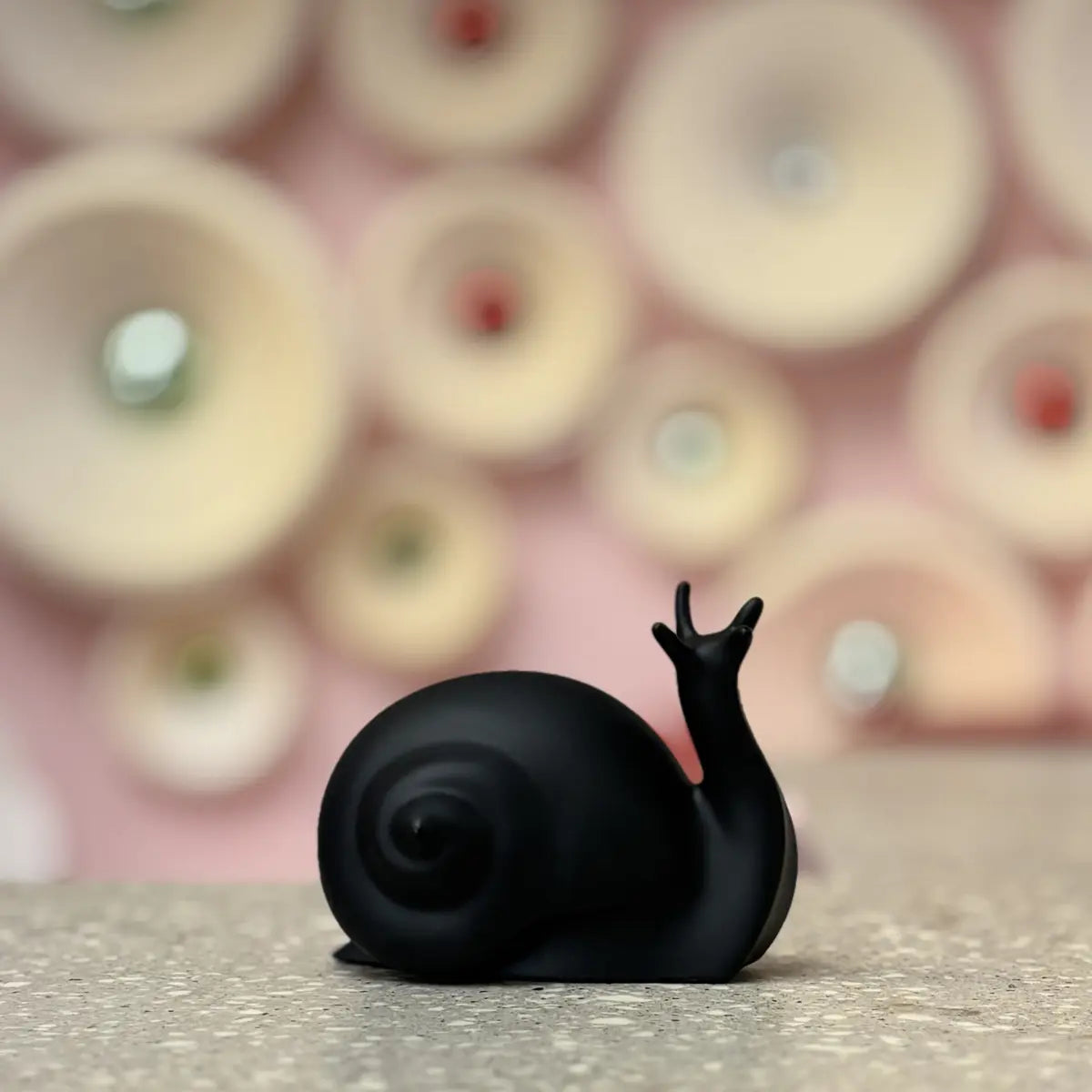 Fermalibri Nina a forma di lumaca nera opaca. Posizionata su una superficie grigia e con sfondo sfuocato.
