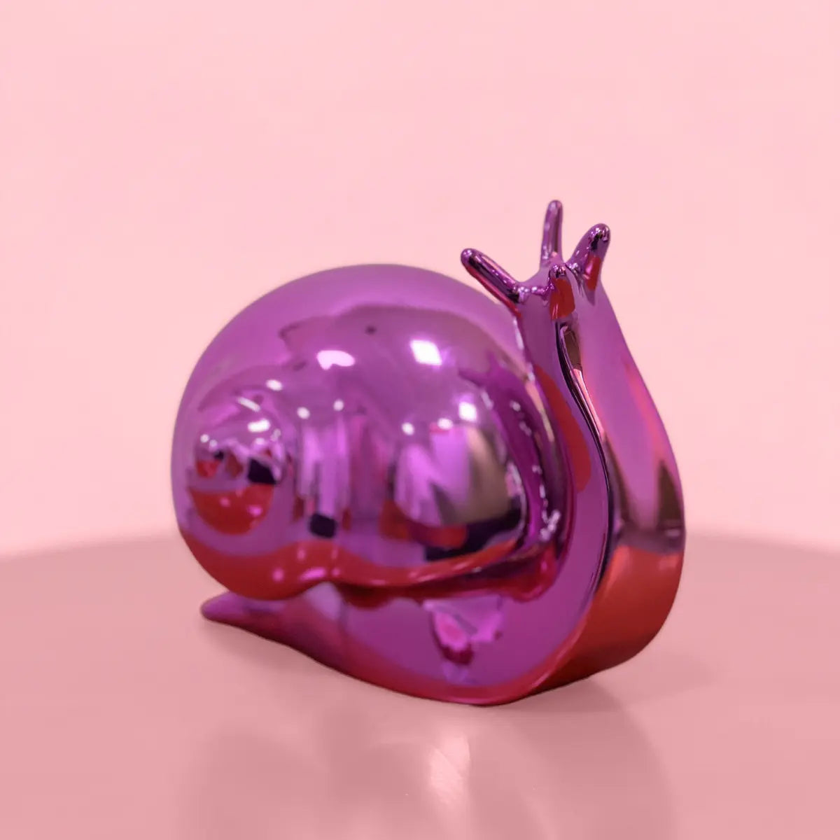 Fermalibri Nina a forma di lumaca Cromato color fucsia visto dall'alto. Posizionato su una superficie rosa sfuocata. 