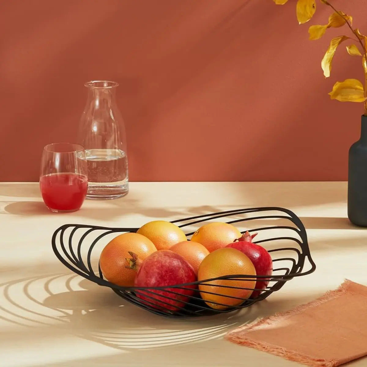 Cestino da frutta in acciaio nero con intagli e forma morbida con arance e melograni
