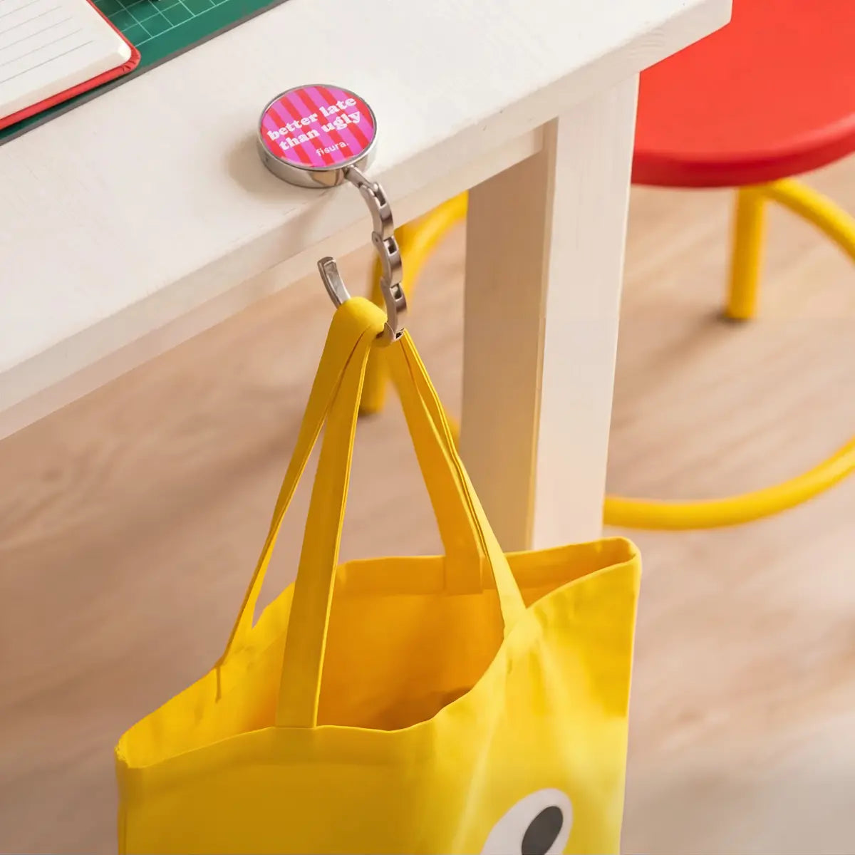 Gancio portaborse in metallo con scritta "Better late than ugly" con borsa gialla appesa