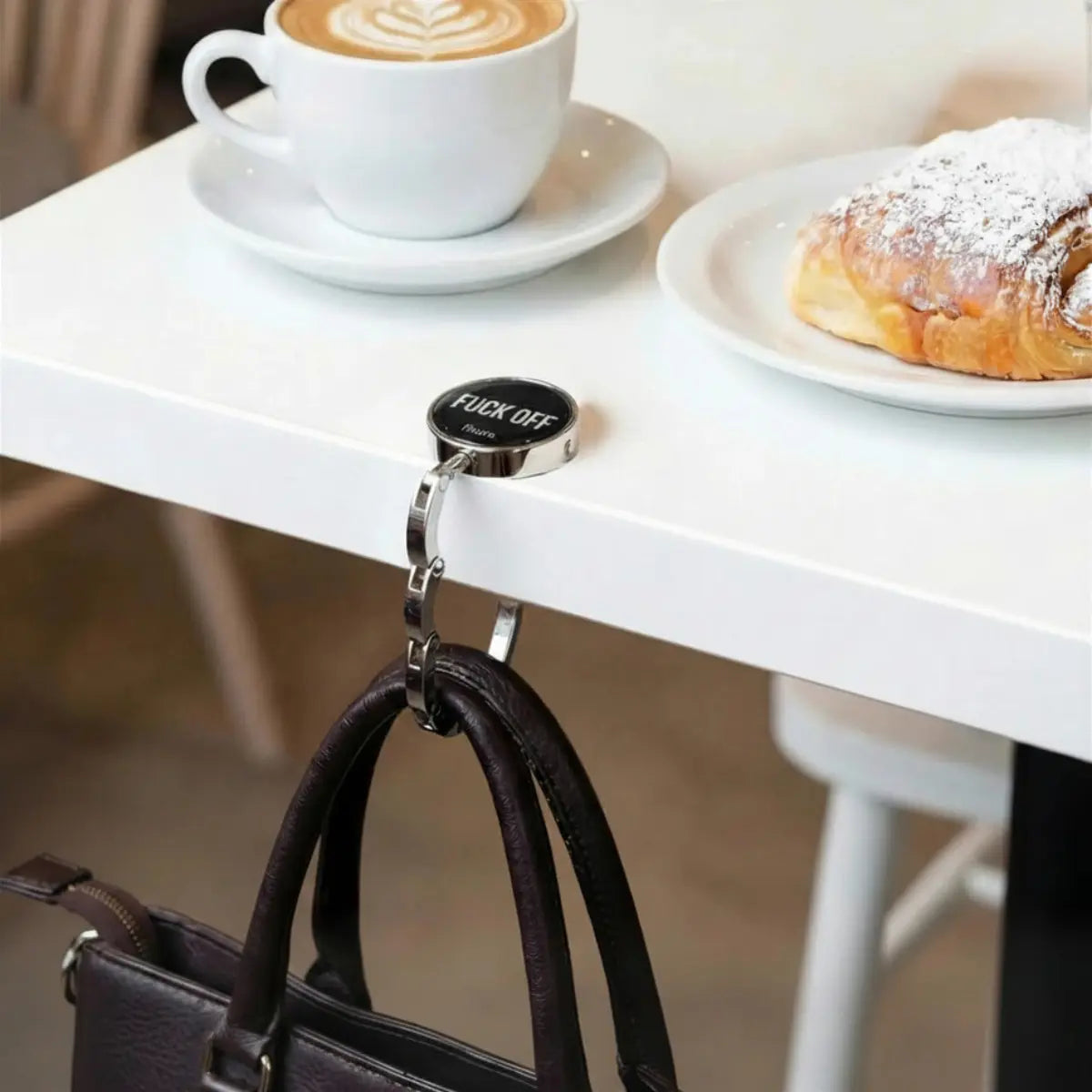 Gancio porta borsa con scritta nera "Fuck off" con una borsa appesa.