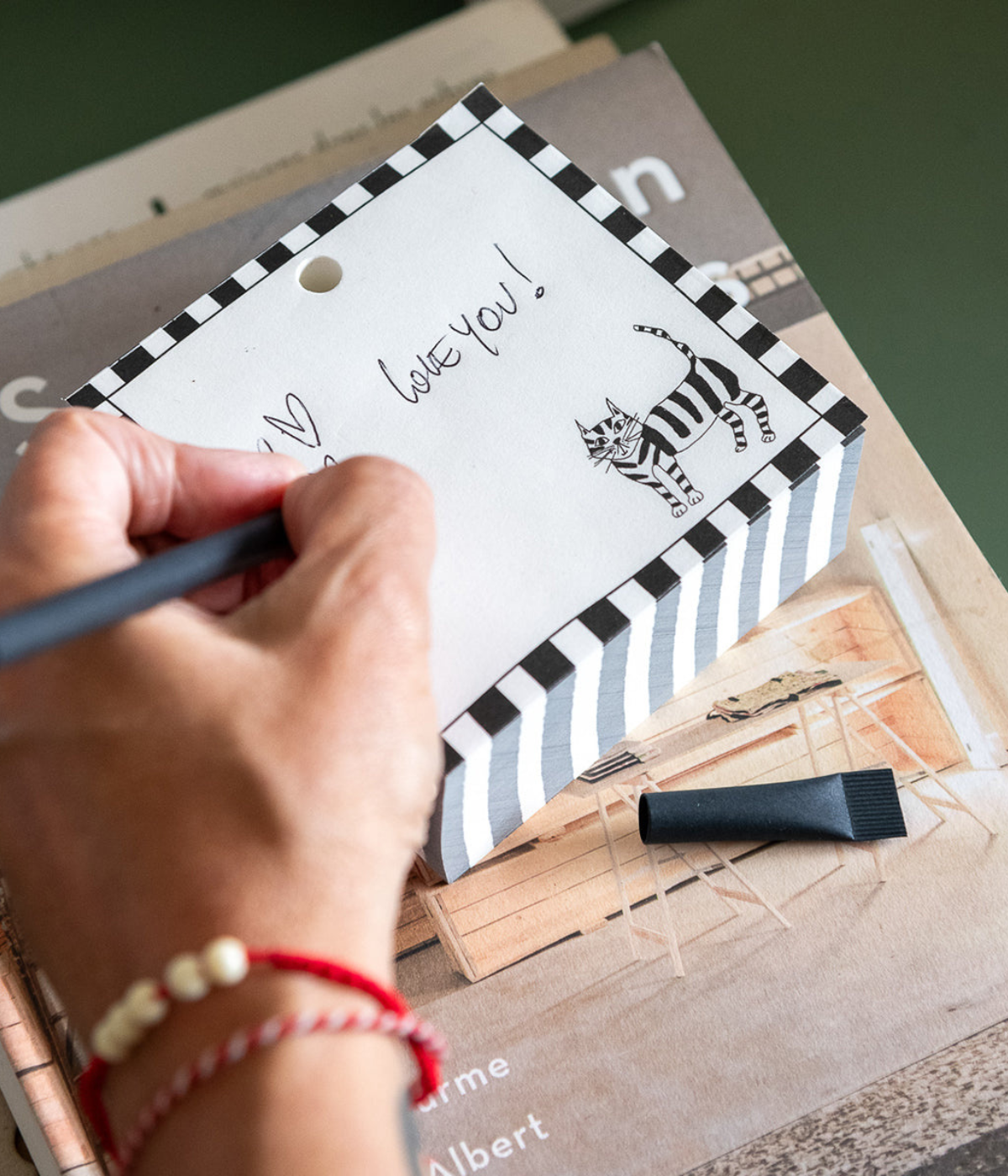 Persona che scrive su Blocknote con gatto nero disegnato. Cornice bianca e nera scritta Love You.