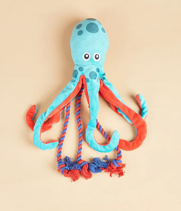 Gioco per cani a forma di polipo. Azzurro e rosso con tentacoli in corda rossi e blu. Sfondo beige.