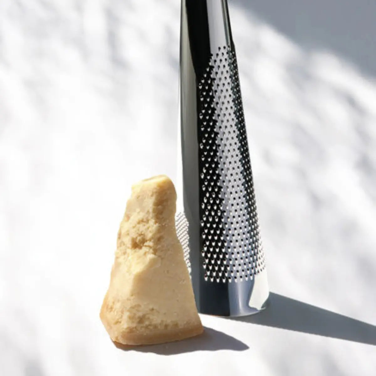 Dettaglio grattugia in acciaio inox vicino a un pezzo di grana