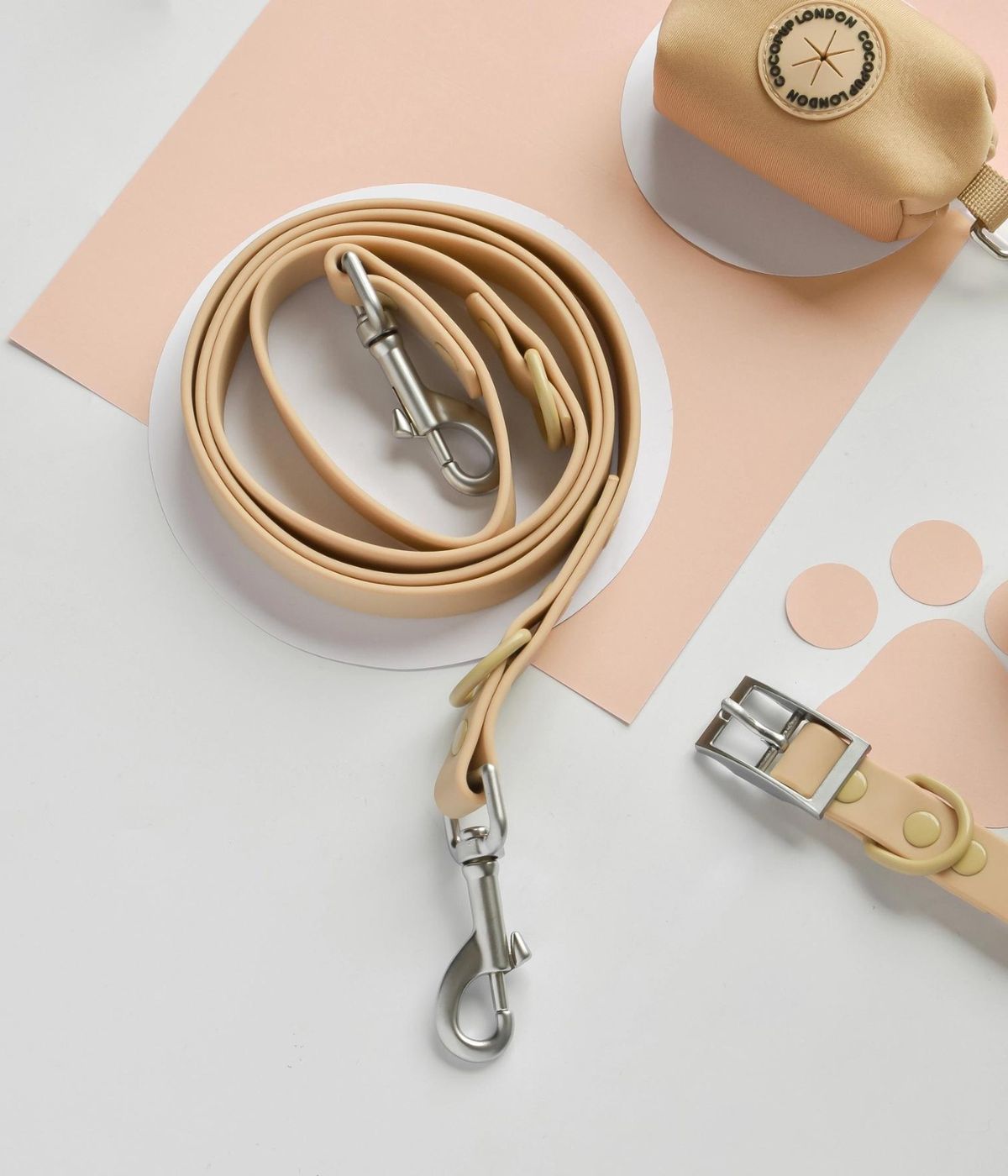 Guinzaglio per cane di colore biscotto arrotolato con moschettone su superficie bianca.