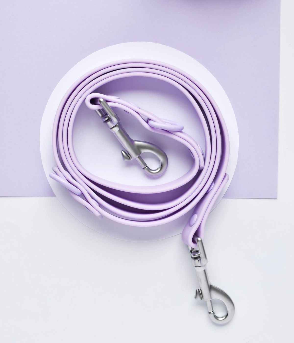 Guinzaglio per cane viola arrotolato su una superficie bianca con moschettoni in acciaio.