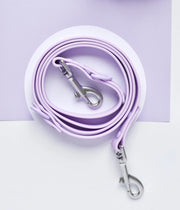 Guinzaglio per cane viola arrotolato su una superficie bianca con moschettoni in acciaio.