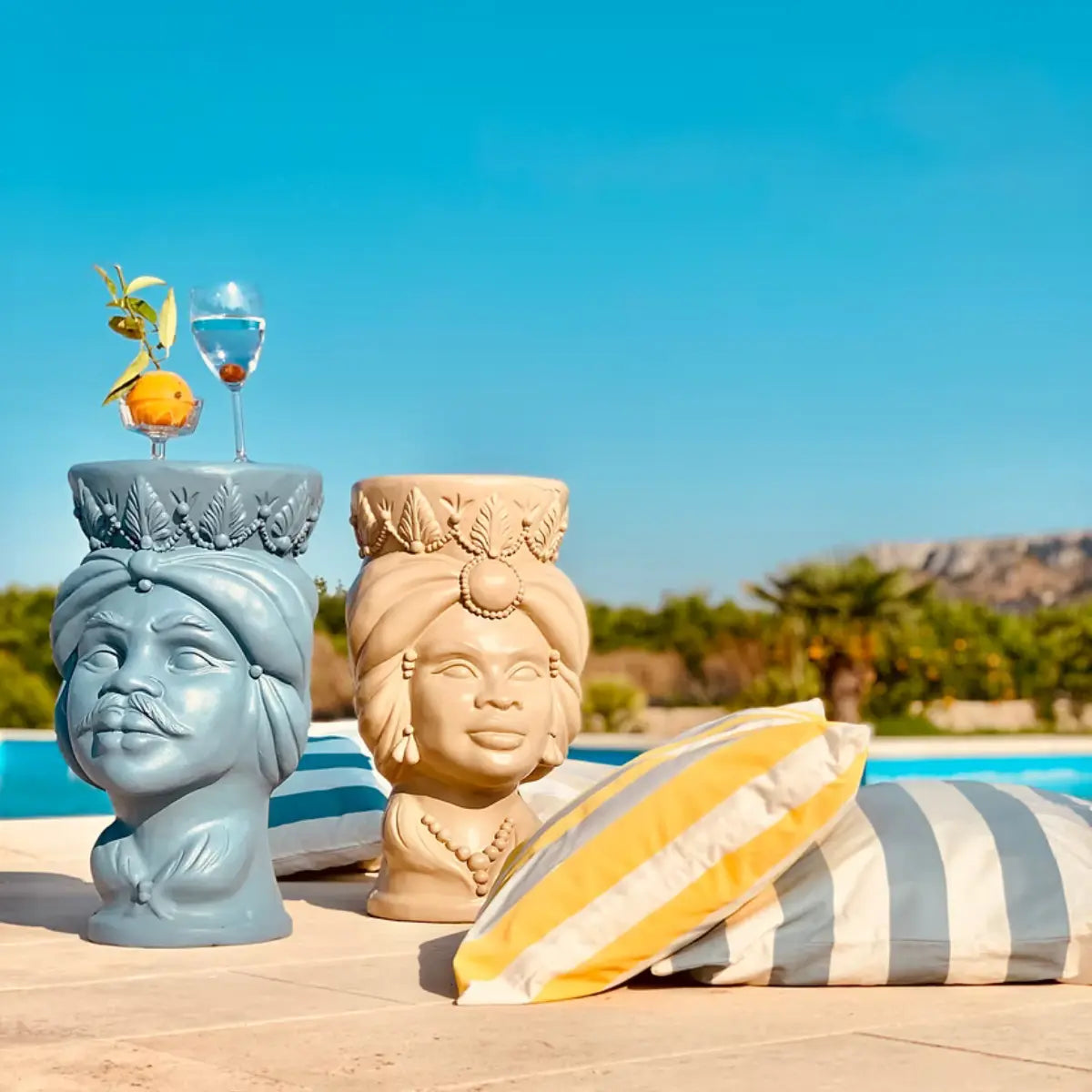 Testa di moro color celeste posizionato a bordo piscina e utilizzato come tavolino su cui sono appoggiati due cocktail