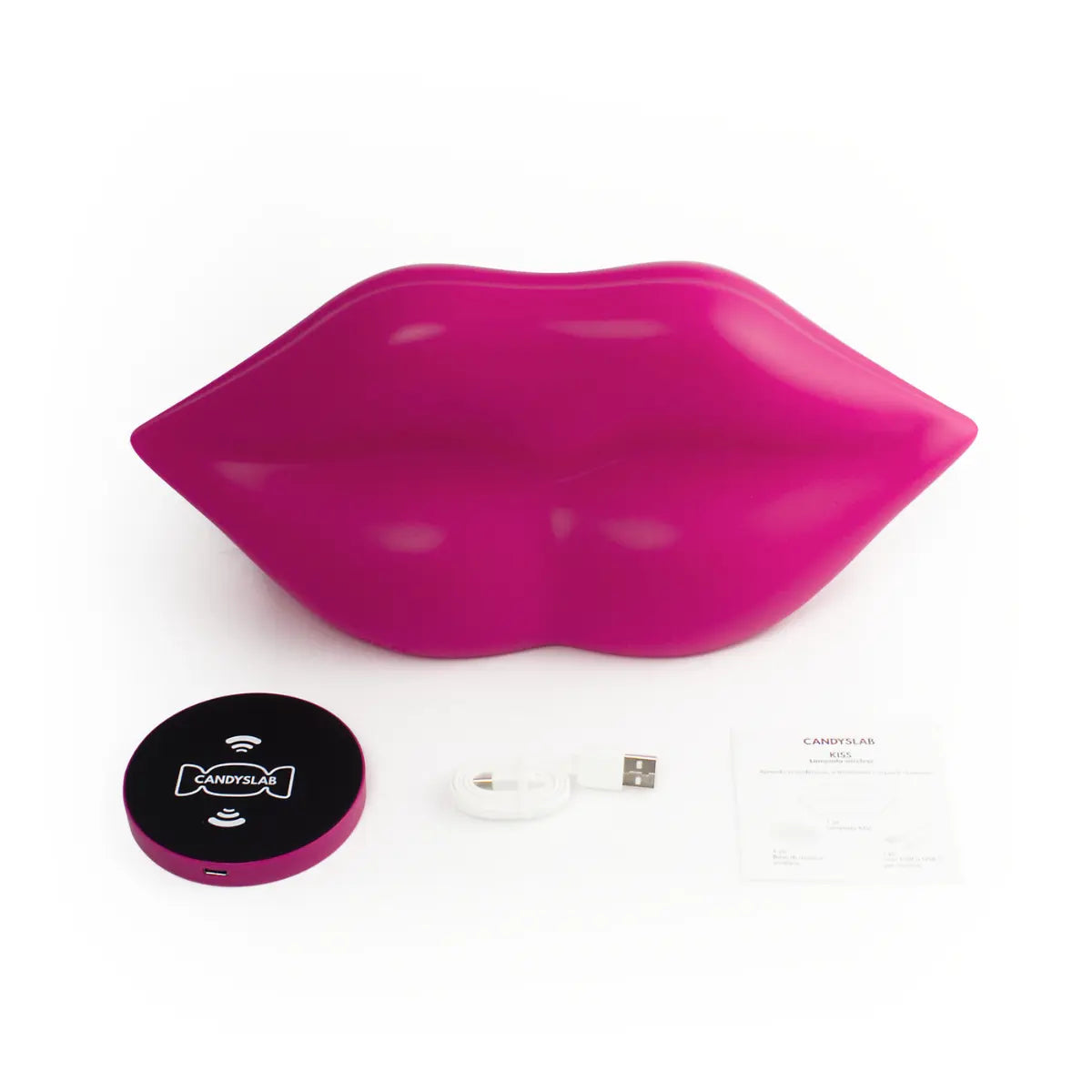 Lampada da tavolo fucsia a forma di labbra. Appoggiati accanto alla lampada tutto ciò che contiene la confezione ovvero la base di ricarica wireless, il caricatore e il foglietto illustrativo. Sfondo bianco