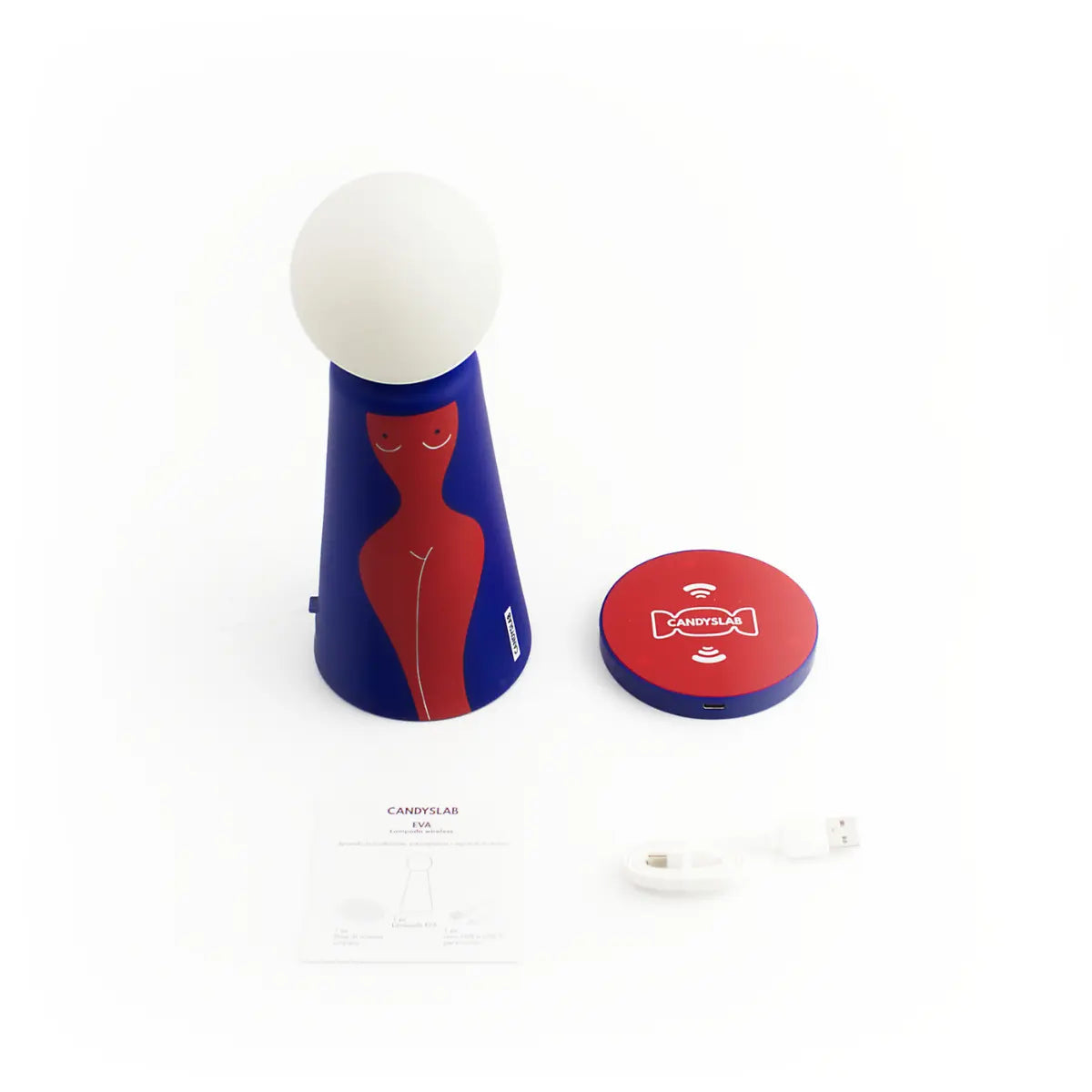 Lampada da tavolo a forma conica con sfera luminosa. Base blu com figura femminile rossa. Posizionato accanto alla lampada la base diricarica wireless, il cavo di ricarica e il libretto d'istruzione. Sfondo bianco 