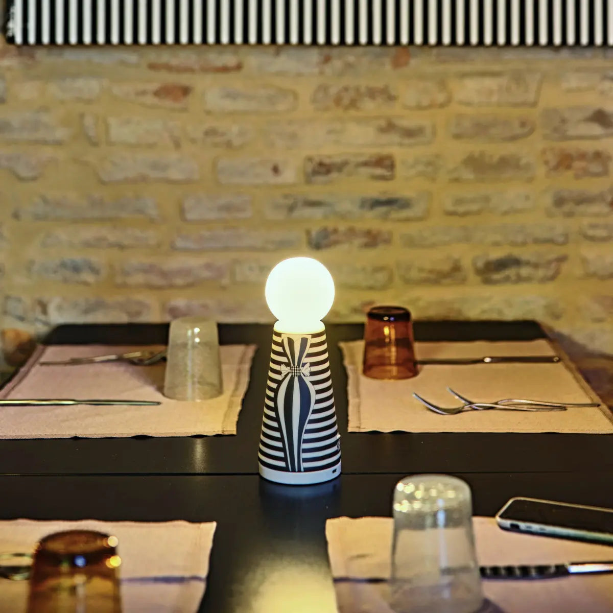 Lampada Eva a righe bianche e nere posizionata su un tavolo apparecchiato. 