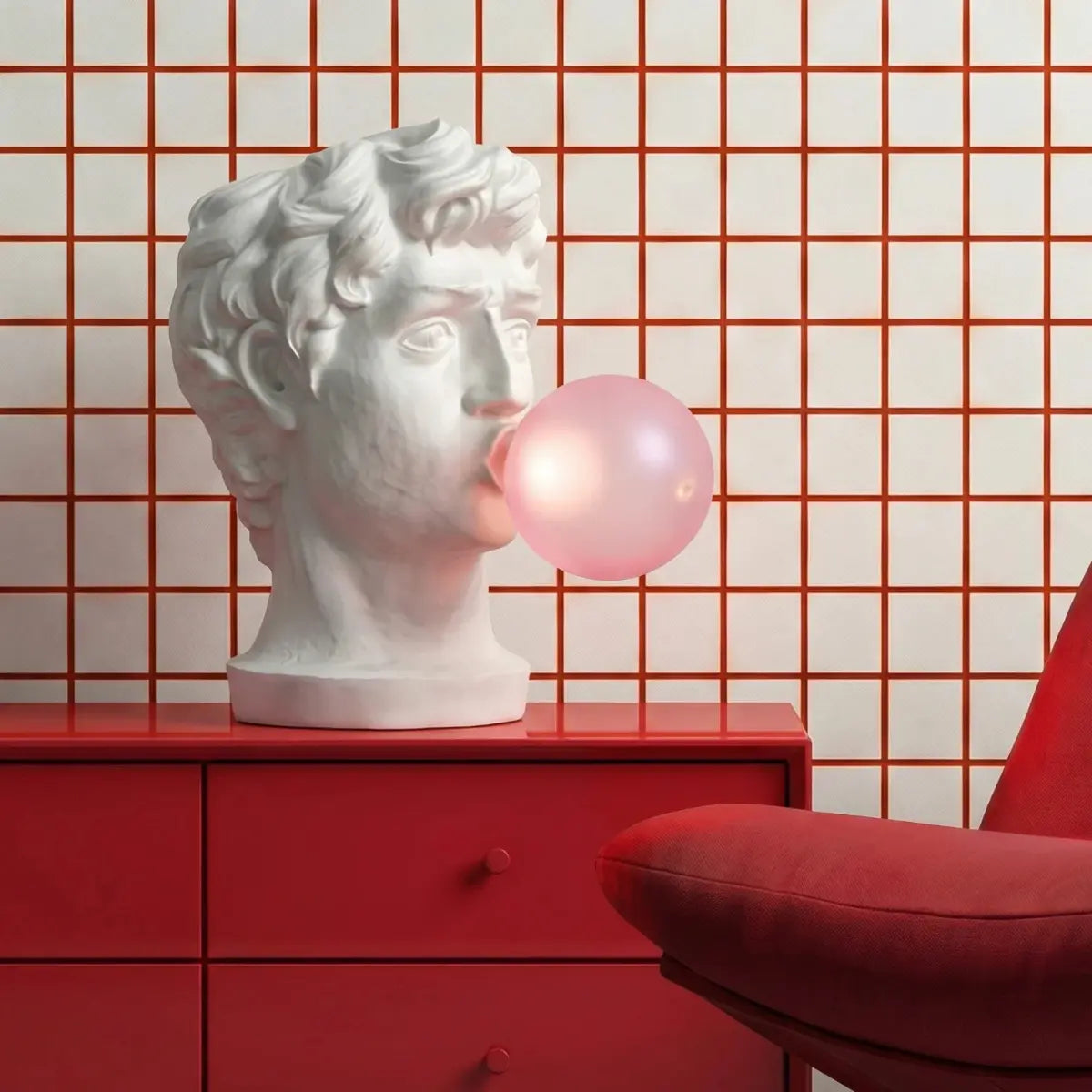 Lampada Wonder di Seletti che rappresenta il viso di un giovane ragazzo fare una bolla di chewimng gum. La lampada è posizionata su un mobile laccato rosso. Lo sfondo è geometrico bianco e rosso