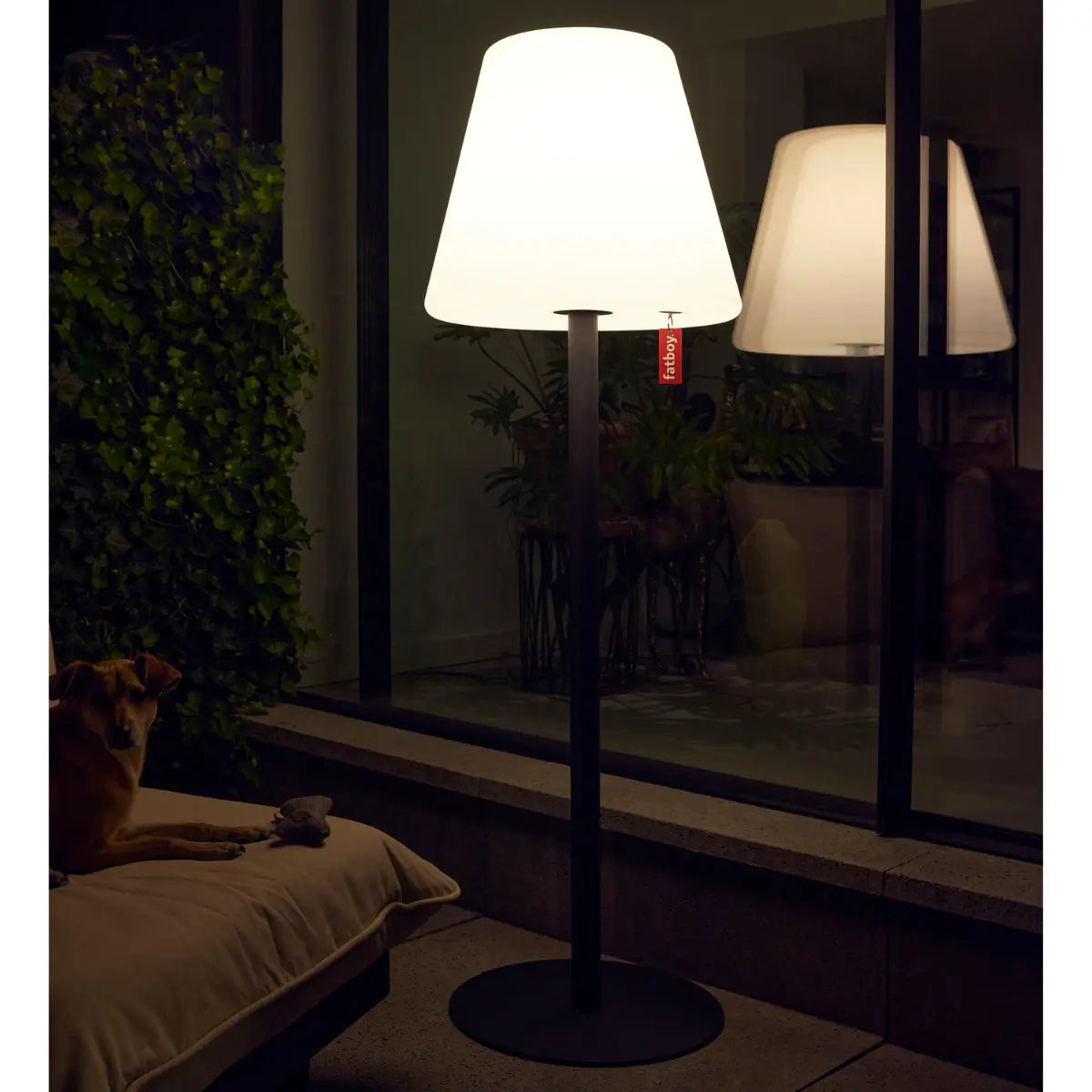 Lampada da terra con paralume bianco e stelo grigio posizionata all'esterno.