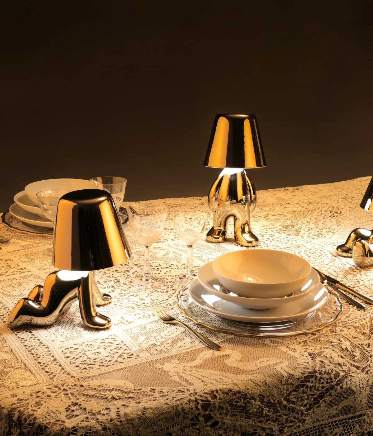 Lampade dorate a forma di personaggi posizionate su una tavola apparecchiata con tovaglia in pizzo