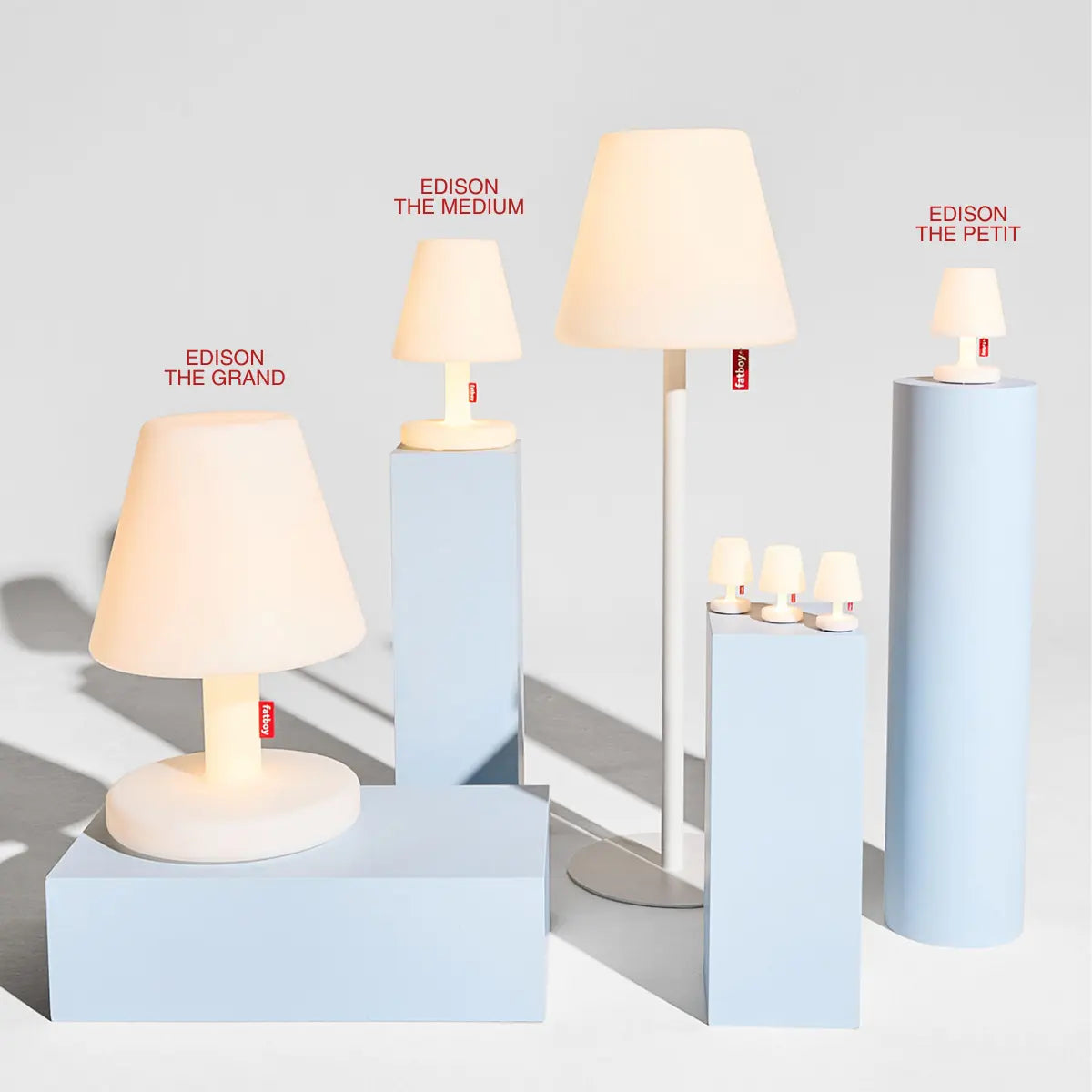 Tutta la famiglia di lampade Edison Fatboy appoggiate su dei piedistalli azzurri. 