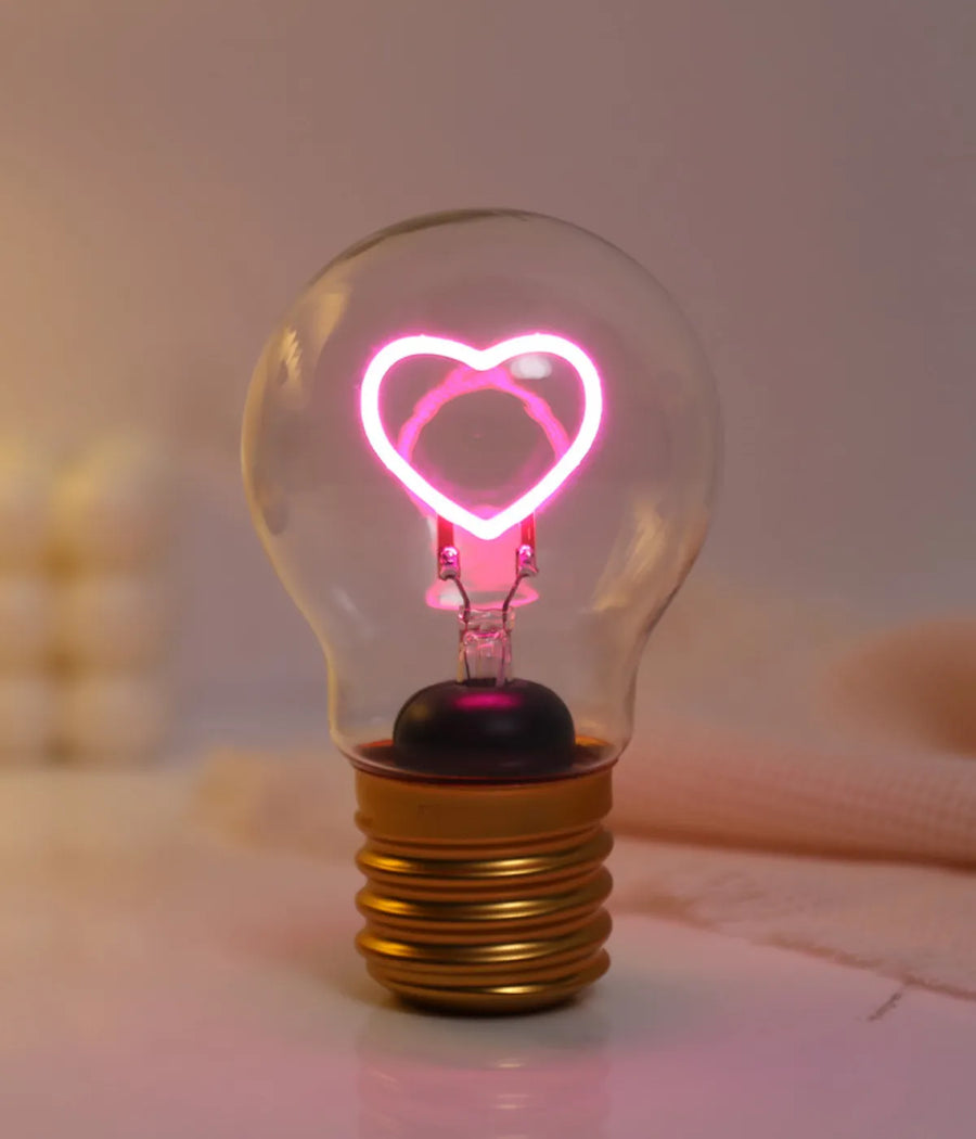 Lampadina da tavolo con led rosa fluo a forma di cuore. Base metallo oro. Sfondo tavolo bianco