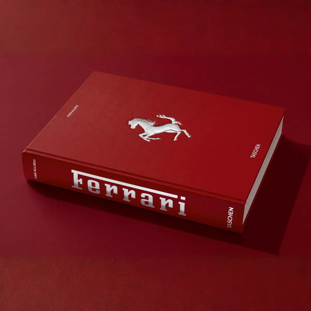 Copertina rossa del libro Ferrari. Cavallo argentato in rilievo e scritte in argento. Sul dorso del libro il logo di Ferrari con effetto argentato. Sfondo rosso