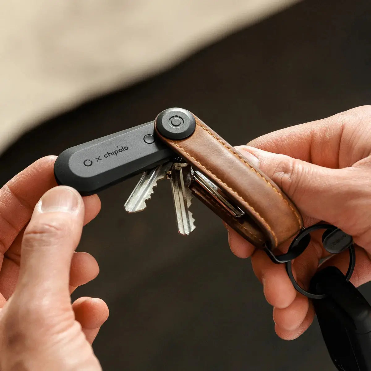 Localizzatore bluetooth nero inserito nel portachiavi compatto Orbitkey in pelle marrone. Mano che estrae il localizzatore