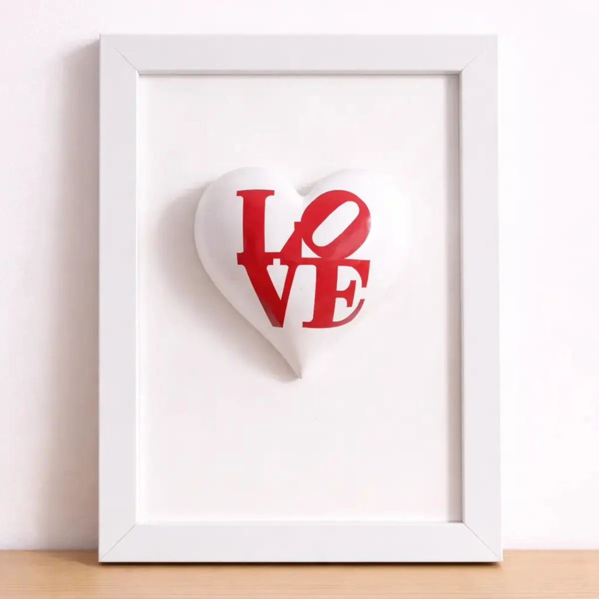 Quadretto CuoreAmore fatto a mano in Italia. Ha una cornice in legno bianca e un cuore in ceramica rosso con una scritta  