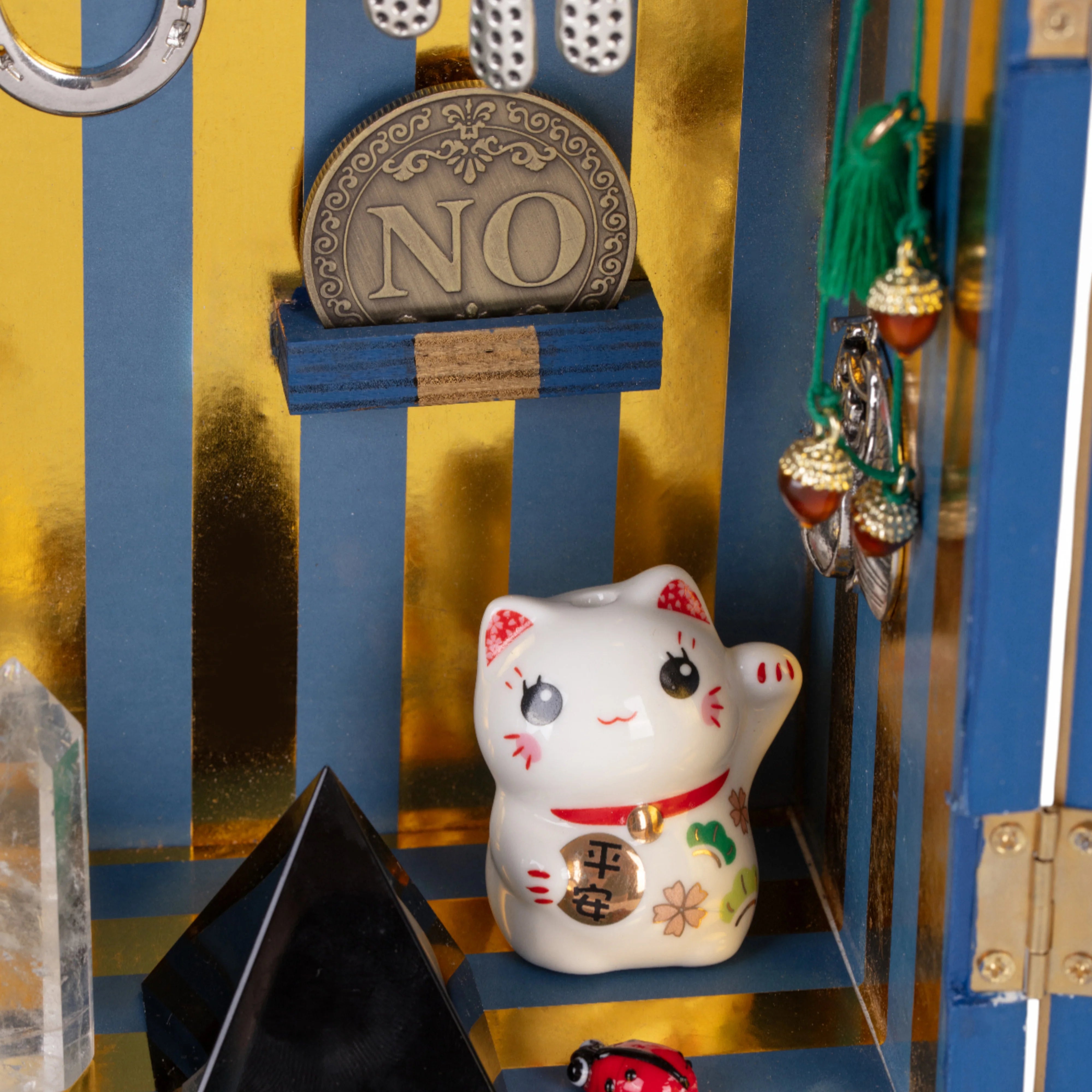 Dettaglio dell'interno del Lucky Temple di Seletti. Ci sono un gattino, una moneta, una coccinella, una piramide nera e dei ciondoli