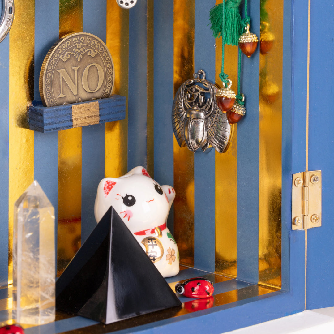 Dettaglio dell'interno del Lucky Temple di Seletti. Ci sono un gattino, una moneta, una coccinella, una piramide nera, un cristallo e dei ciondoli con le ghiande.