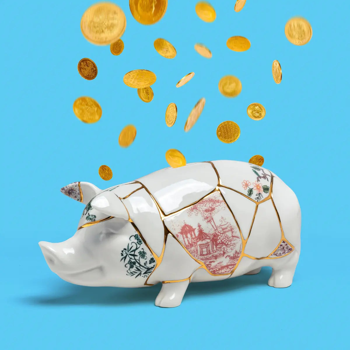 Salvadanaio a forma di mailino in porcellana con dettagli in oro. Realizzato con la tecnica giapponese del Kintsugi. Sfondo azzurro e monete d'oro che cadono