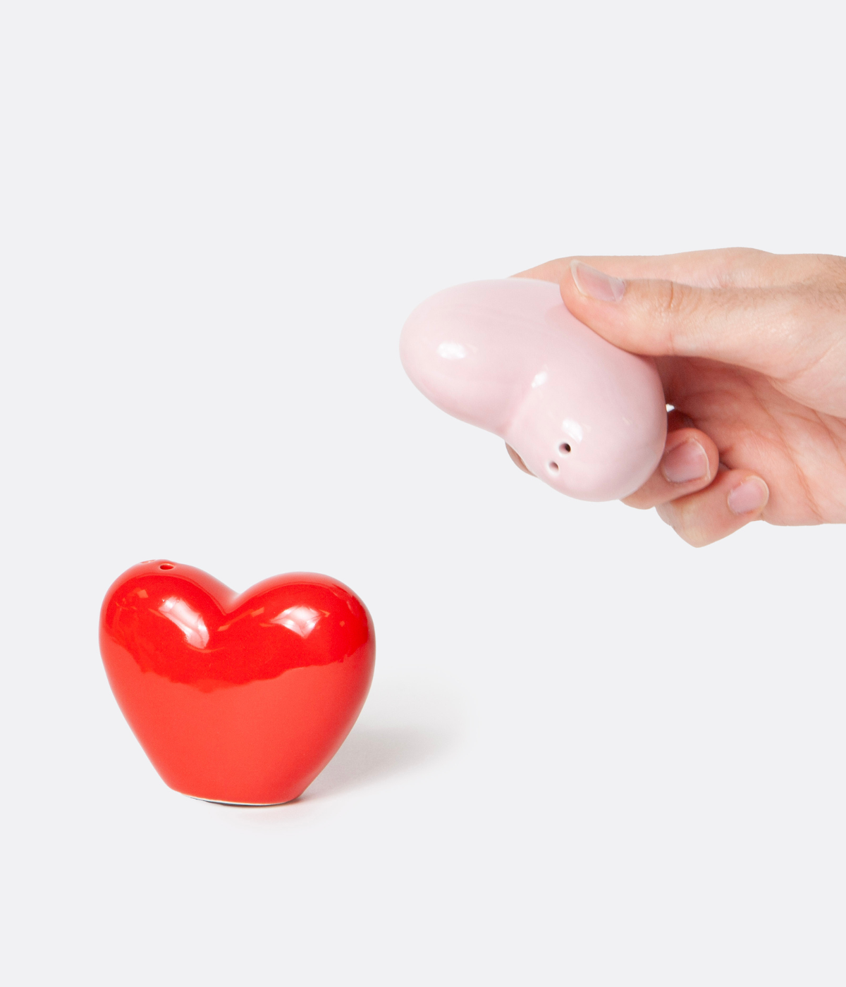 Due cuori in ceramica rosso e rosa tenuto da una mano. Fori per uscita sale e pepe. Sfondo bianco