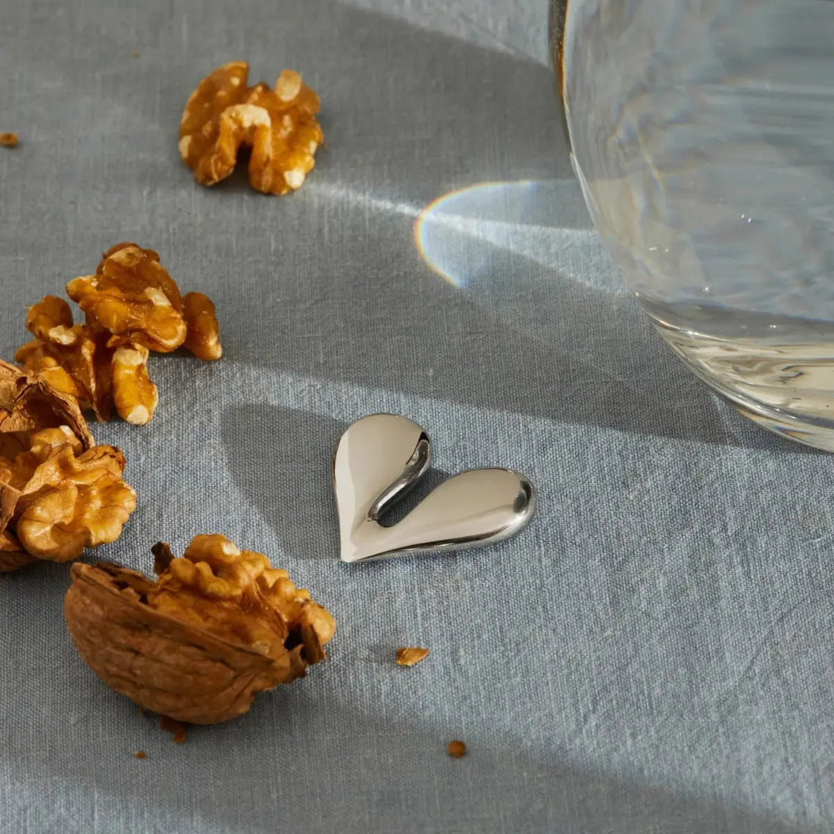 Aprinoci Nut Splitter di Alessia acciaio inox appoggiato su un tavolo con tovaglia azzurra. Sul tavolo sono posizionate delle noci aperte.