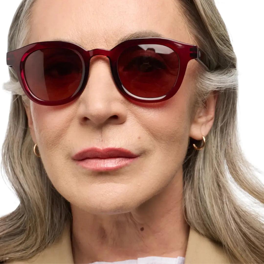 Donna che indossa occhiale da sole montatura bordeaux con lente rosa. Sfondo bianco