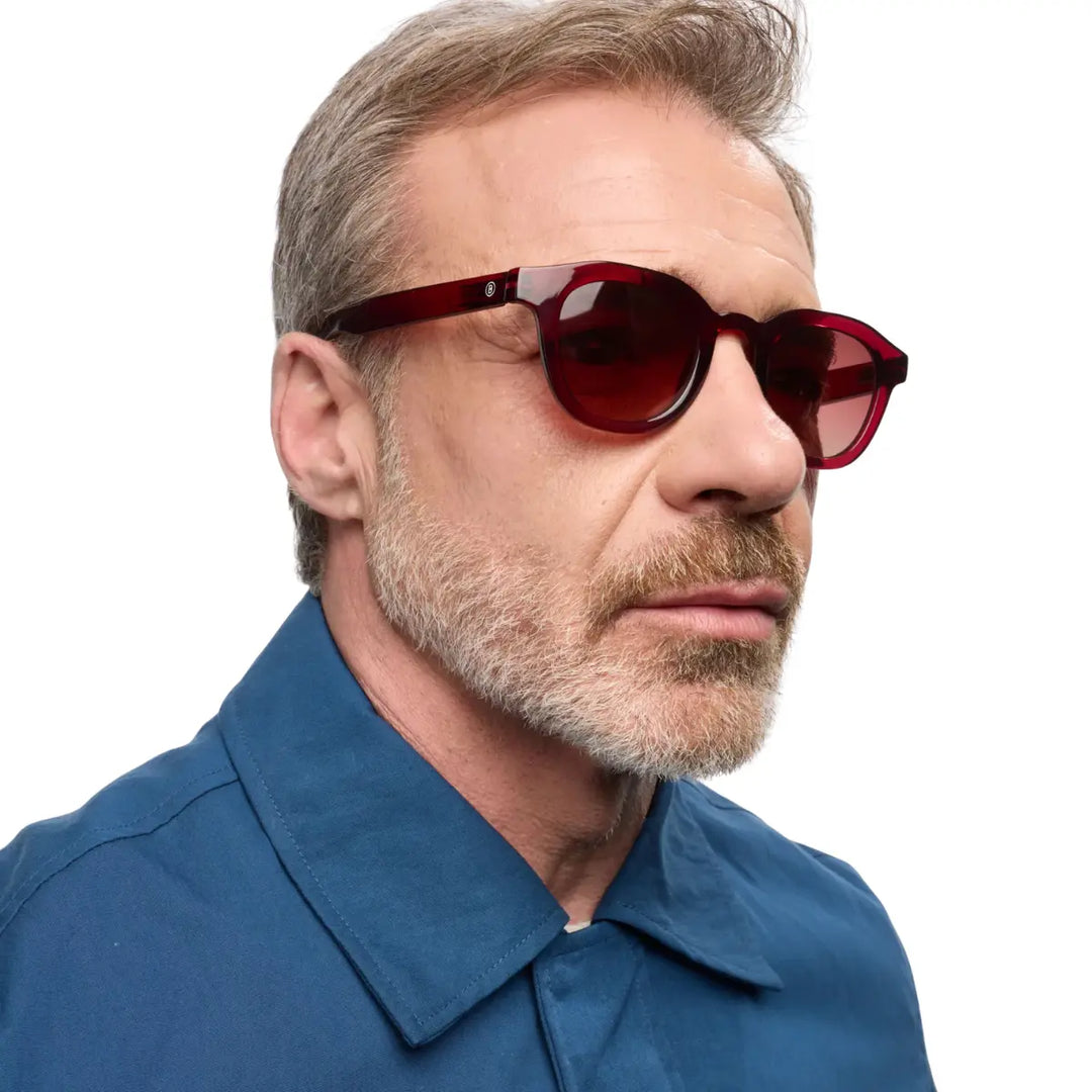 Uomo che indossa occhiale da sole montatura bordeaux con lente rosa. Sfondo bianco