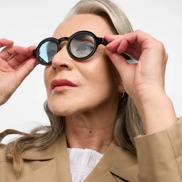 Donna che indossa occhiale da sole montatura nera con lente azzurra.